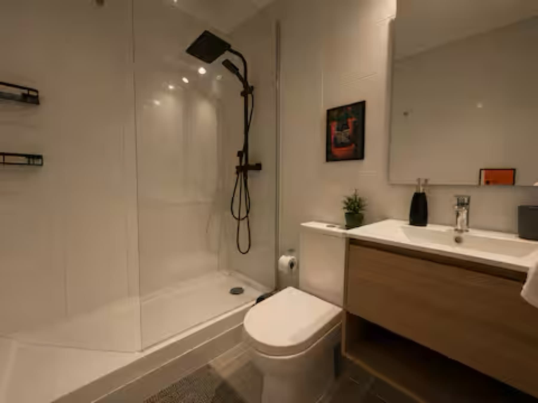 Baño con mampara de cristal, grifería negra y mueble de madera