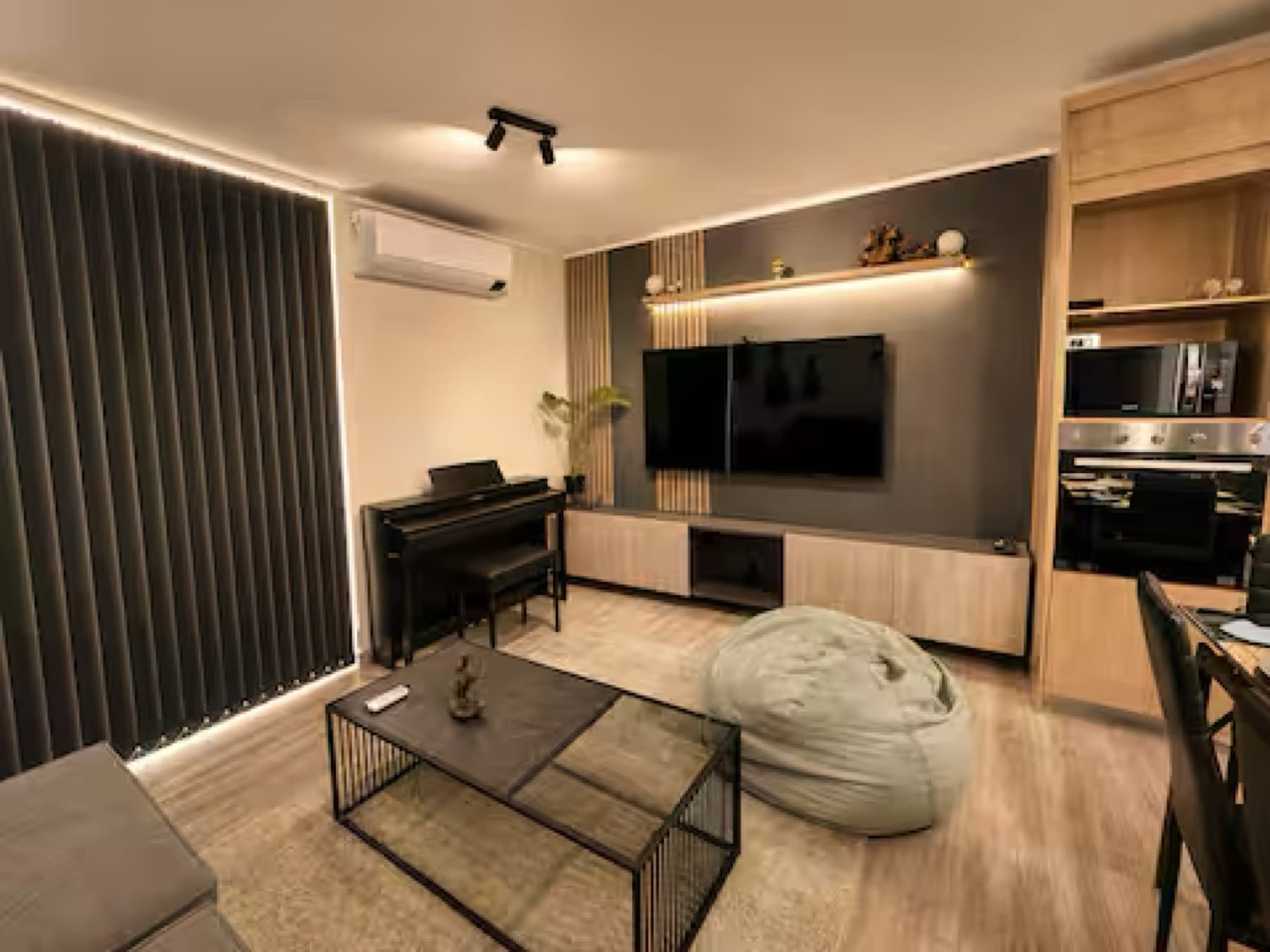 Living con piano, televisor y luz cálida en un departamento administrado por Luxel